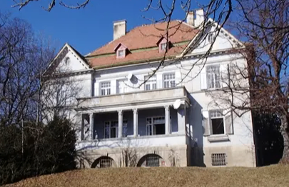 Ein großes weißes Haus mit einem roten Dach und vielen Fenstern, umgeben von Bäumen und Gras.