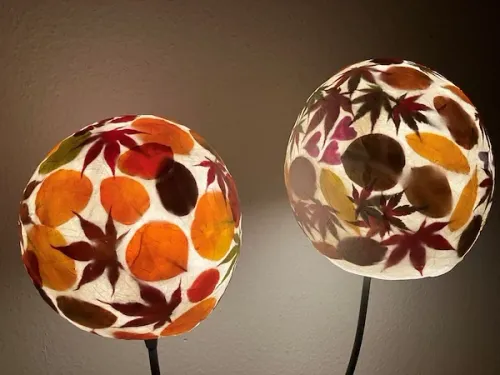 Zwei kugelförmige Lampen, jeweils mit einer Vielzahl von Herbstblättern verziert, sind an einer grauen Wand montiert.