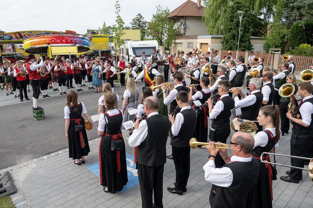 Eine große Band spielt auf der Straße in traditioneller Kleidung. Sie stehen vor einem Gebäude mit einem farbenfrohen Karussell in der Nähe.