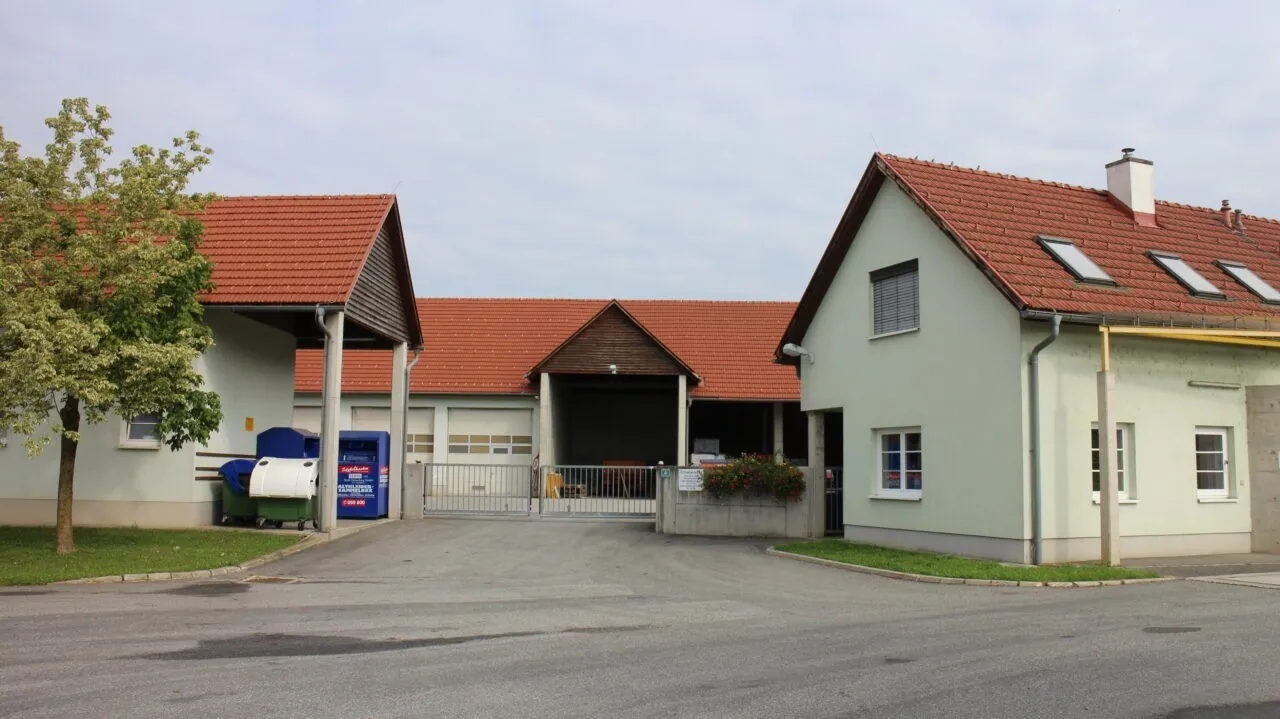 Ein Wohngebiet mit zwei Häusern und Garagen, einem Mülleimer und einem geschlossenen Tor davor.