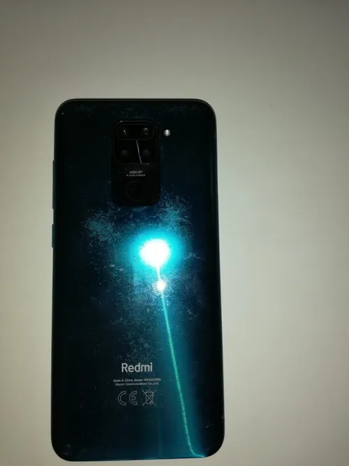 Die Rückseite eines Redmi-Smartphones mit türkisfarbener Oberfläche und Kamera-Setup wird gezeigt. Der Markenname ist prominent angebracht, und ein Lichtreflex ist sichtbar.