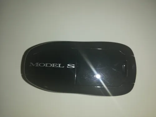Eine schwarze kabellose Maus mit dem Aufdruck MODEL S. Sie liegt auf einer weißen Oberfläche.