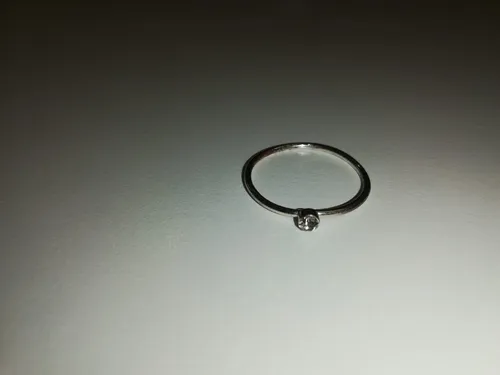 Ein Silberring mit einem kleinen Diamanten in der Mitte wird auf einer schlichten Oberfläche gezeigt.
