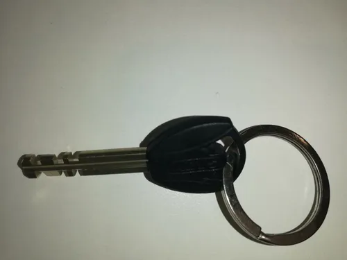 Eine Nahaufnahme eines schwarzen Schlüssels mit einem silbernen Ring, der auf einer weißen Oberfläche liegt. Der Schlüssel hat einen flachen Kopf und ein Stück Metall.