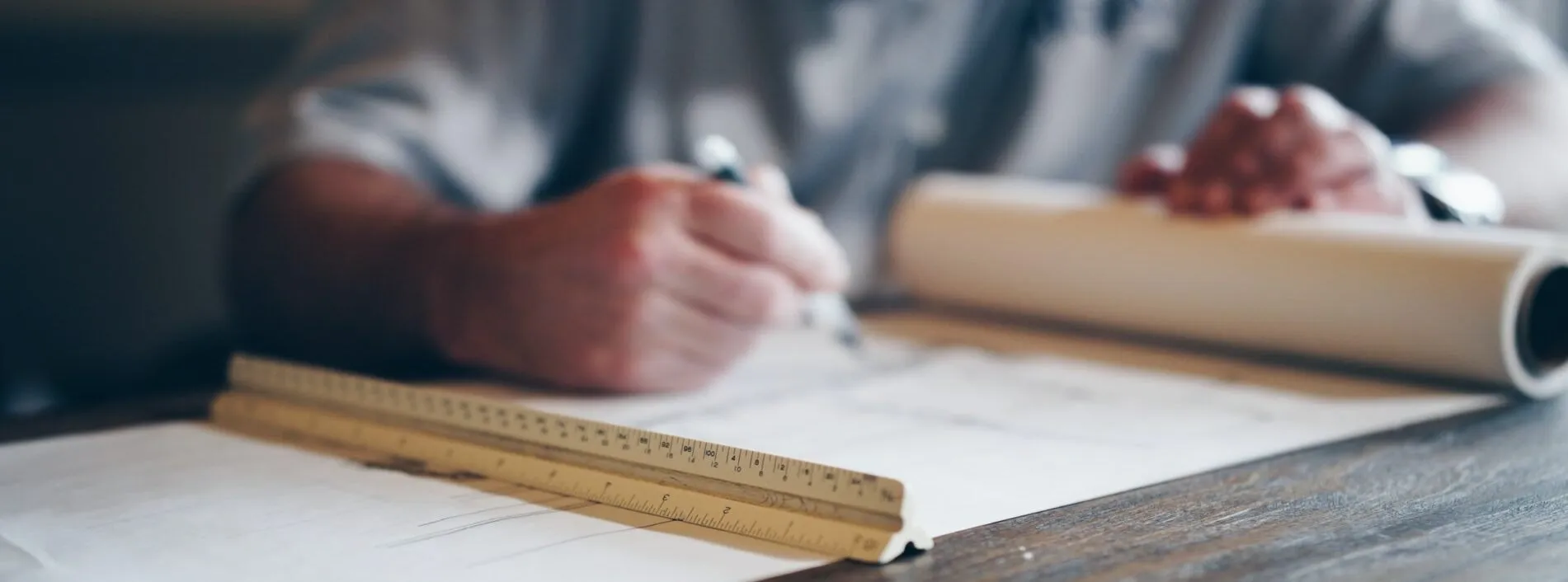 Eine Person zeichnet mit einem Stift auf einem Blatt Papier und verwendet ein Lineal. Das Lineal liegt auf dem Papier, und die Hand der Person ist verschwommen.