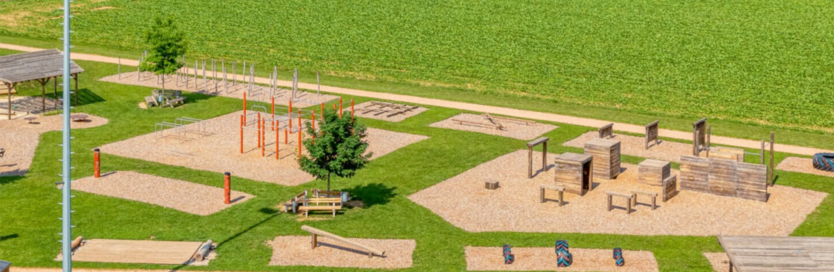 Eine Vogelperspektive eines Spielplatzes mit verschiedenen Geräten wie Rutschen und Wippen auf einem Rasenfeld.