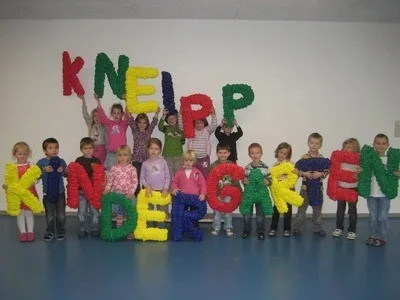 Eine Gruppe von Kindern posiert für ein Foto mit Buchstaben, die Kneipp Kindergarten buchstabieren, und halten bunte Buchstaben hoch.