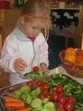 Ein kleines Mädchen in einer weißen Jacke bereitet in einem Klassenzimmer einen Salat aus Tomaten, Gurken und Karotten zu.