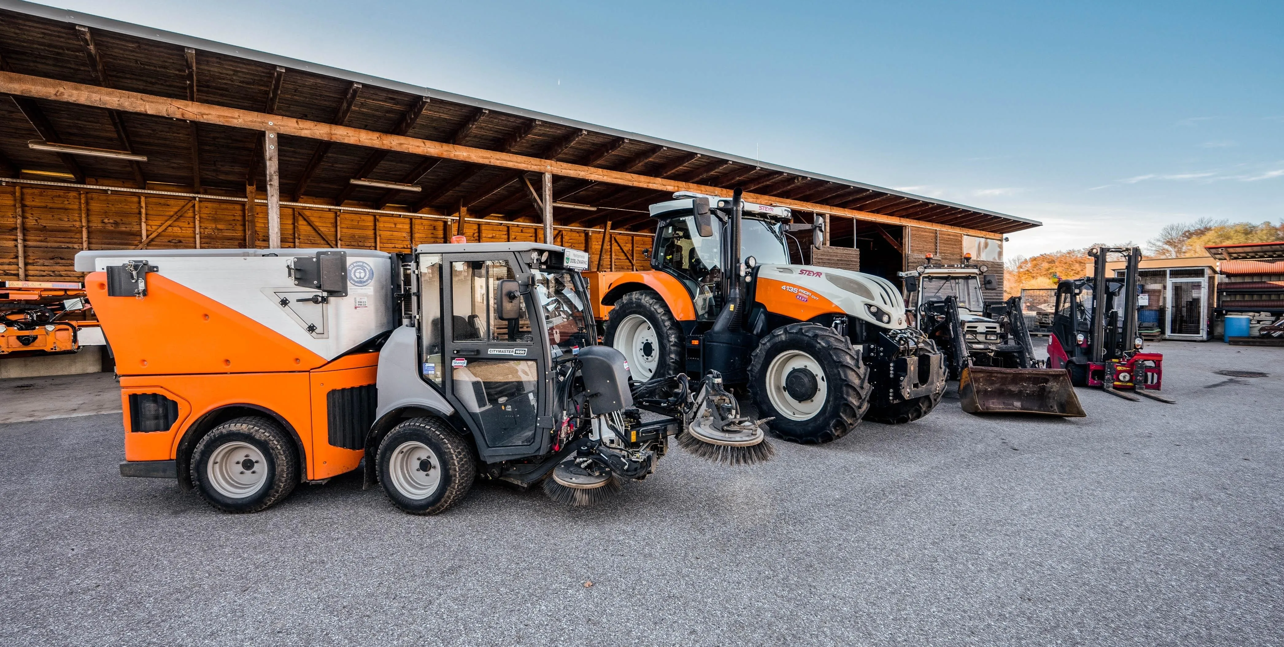 Ein Traktor mit einer Bürstenvorrichtung ist vor einer Scheune geparkt, dahinter steht ein weiterer Traktor.