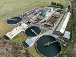 Luftaufnahme einer großen Kläranlage mit mehreren großen Tanks und Gebäuden in ländlicher Umgebung.
