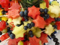 Eine Nahaufnahme eines Obstsalats mit sternförmigen Wassermelonen-, Ananas- und Blaubeerstücken auf Spießen.
