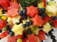 Eine Nahaufnahme eines Obstsalats mit sternförmigen Wassermelonen-, Ananas- und Blaubeerstücken auf Spießen.