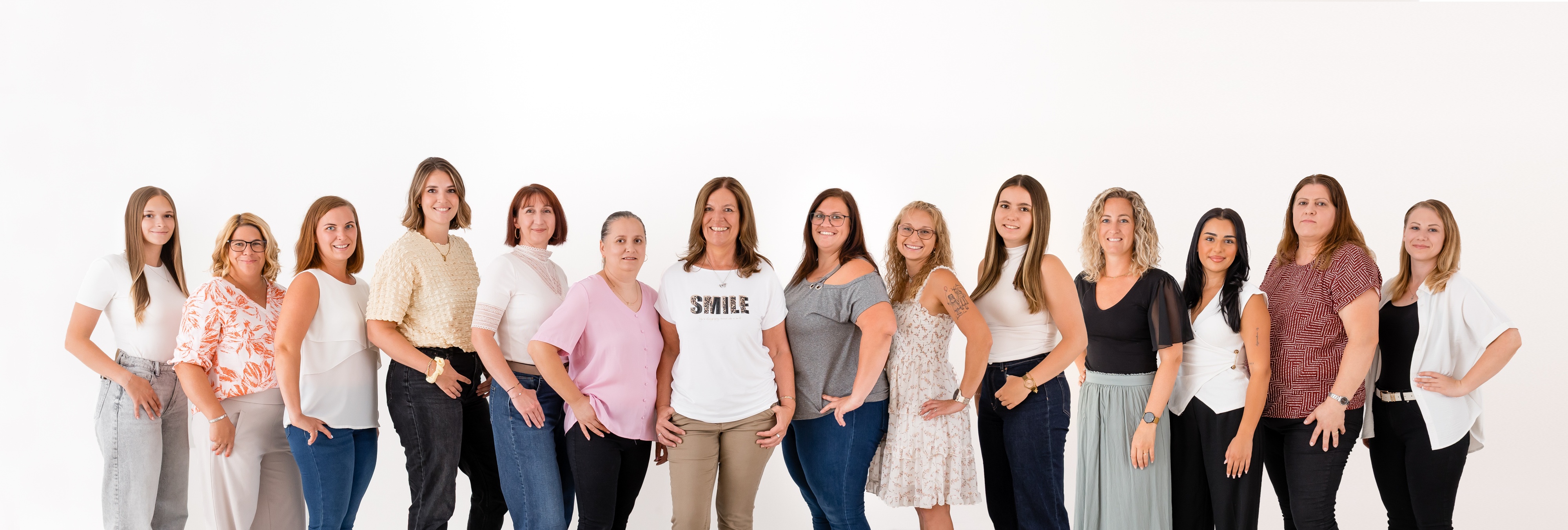 Eine Gruppe von Frauen steht zusammen, lächelt und posiert für ein Foto. Sie tragen verschiedenfarbige Kleidung und stehen in einer Reihe.