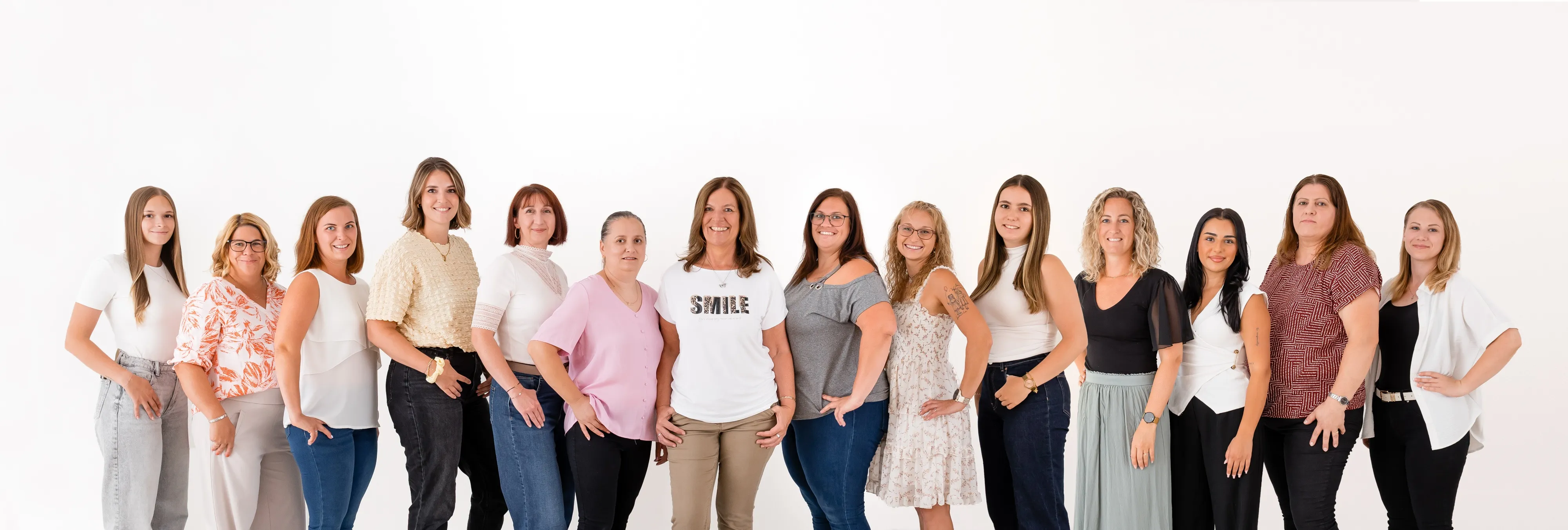 Eine Gruppe von Frauen steht zusammen, lächelt und posiert für ein Foto. Sie tragen verschiedenfarbige Kleidung und stehen in einer Reihe.