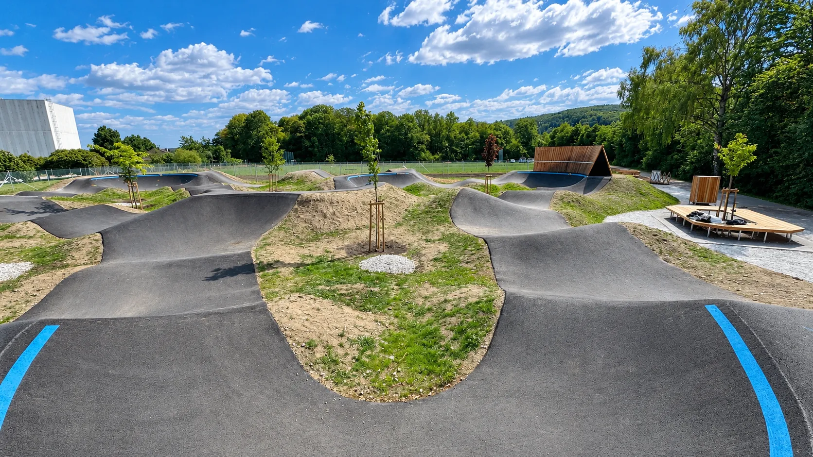Ein Outdoor-Skatepark mit verschiedenen Rampen und Kurven, umgeben von Bäumen und Gras.