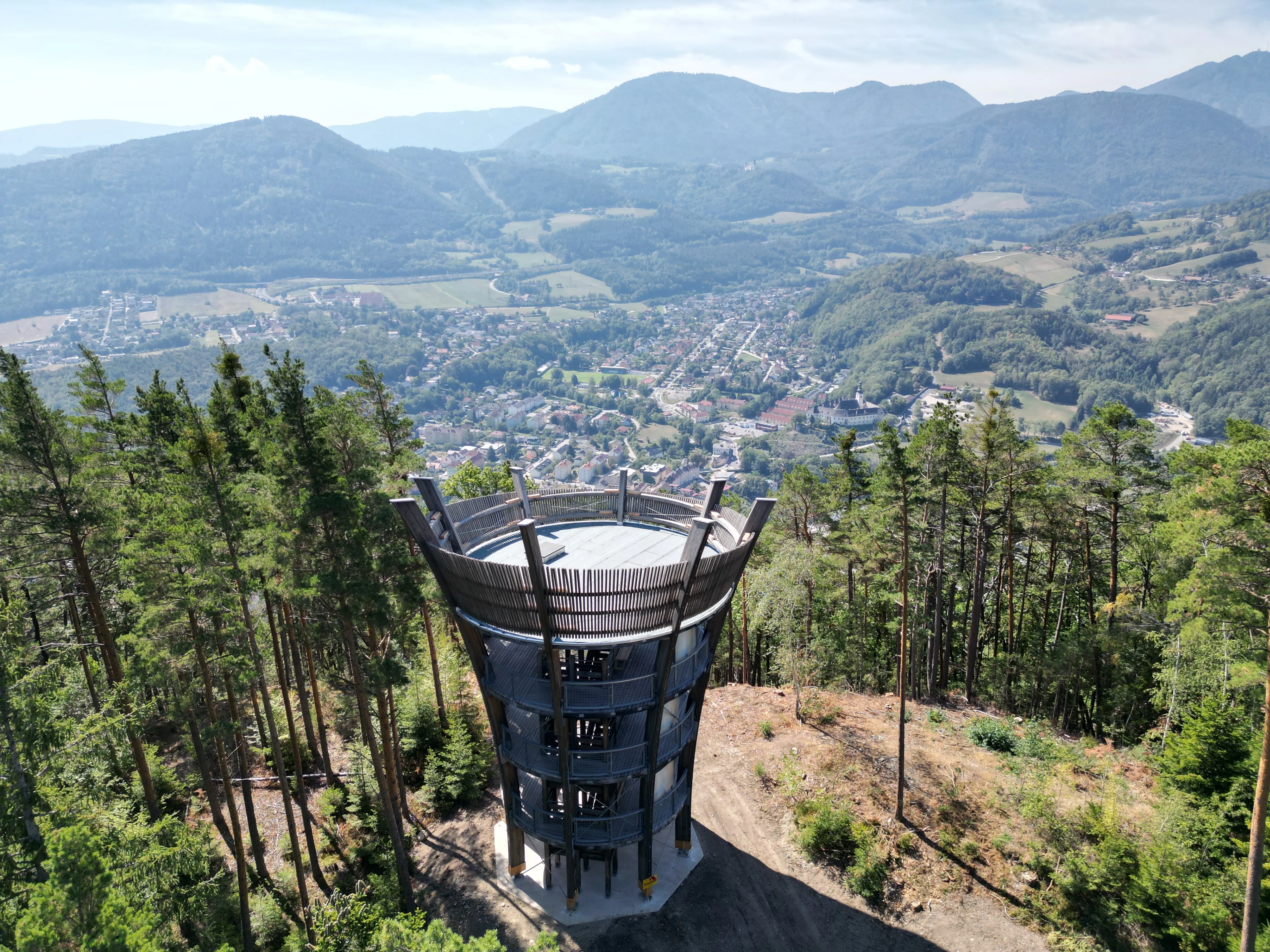 Ein Luftbild eines hohen Turms mit einer Wendeltreppe, umgeben von einem üppigen grünen Wald und einer Stadt in der Ferne.