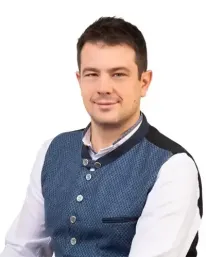 Ein Mann in einem weißen Hemd und einer blauen Weste lächelt und posiert für ein Foto.