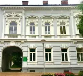 Ein großes weißes Gebäude mit mehreren gewölbten Fenstern und einem großen Eingang. Die Fassade ist mit klassischen architektonischen Details verziert.