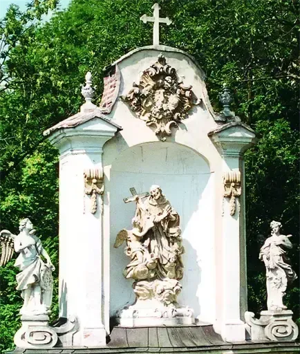 Eine Barock-Skulpturennische mit einem Kreuz auf der Spitze. Sie zeigt eine zentrale Statue eines Mannes und eines Kindes, flankiert von zwei Engelstatuen.