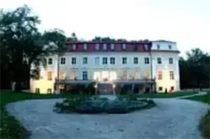 Ein großes weißes Gebäude mit vielen Fenstern und einem roten Dach ist nachts beleuchtet und von Bäumen und Gras umgeben.