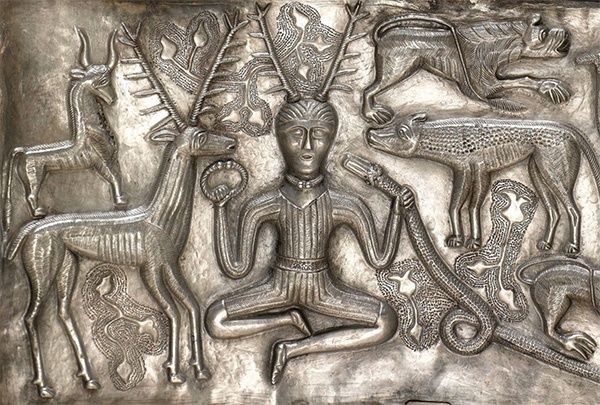 Eine silberne Reliefdarstellung einer sitzenden Figur, umgeben von verschiedenen Tieren, darunter Hirsche, ein Löwe und eine Schlange. Die Figur trägt eine Krone und hält ein kreisförmiges Objekt.