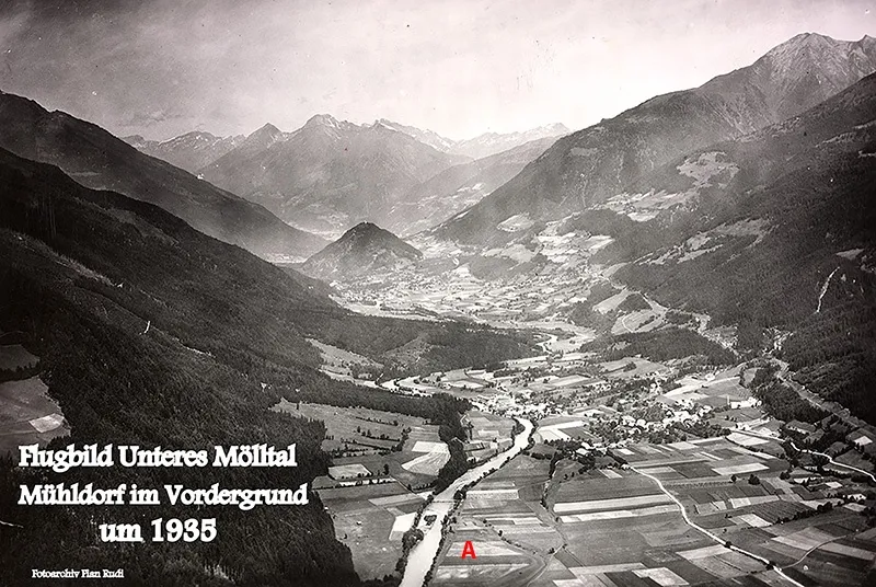 Eine Schwarz-Weiß-Luftaufnahme des Unteres Mölltal-Tals mit einem Dorf im Vordergrund, datiert um 1935. Das Bild zeigt eine Berglandschaft mit einem Fluss, der sich hindurchschlängelt, und einem Label, das auf einen bestimmten Bereich 'A' zeigt.