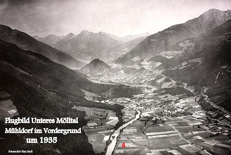 Eine Schwarz-Weiß-Luftaufnahme des Unteres Mölltal-Tals mit einem Dorf im Vordergrund, datiert um 1935. Das Bild zeigt eine Berglandschaft mit einem Fluss, der sich hindurchschlängelt, und einem Label, das auf einen bestimmten Bereich 'A' zeigt.