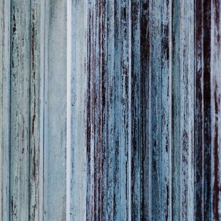 Eine Nahaufnahme von verwitterten blauen Holzsäulen mit sichtbaren Kratzern und Verfärbungen.