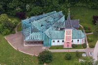 Ein Luftbild einer Kirche mit grünem Dach und einem Turm, umgeben von einem grünen Rasen und Bäumen.