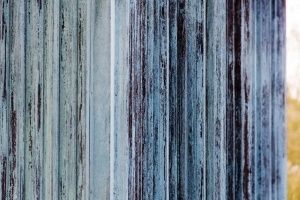 Nahaufnahme eines verwitterten, vertikal ausgerichteten blauen und weißen Holzpanels mit teilweise abgeblätterter Farbe.