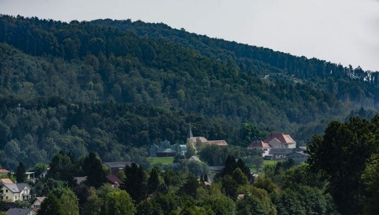 Eine Hügelstadt mit einer Kirche in der Mitte, umgeben von Bäumen und Häusern unter einem klaren Himmel.