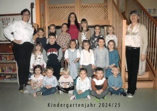Ein Gruppenfoto von Kindergartenkindern und ihren Lehrern aus dem Jahr 2024/25, aufgenommen vor einer Treppe mit einer Gitarre in der Nähe.