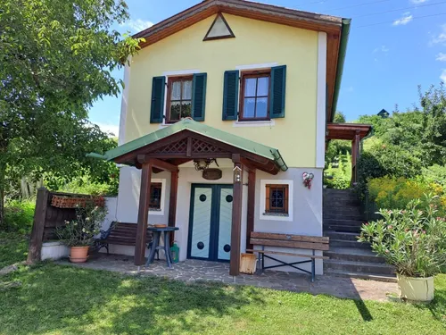 Ein zweistöckiges Haus mit gelber Außenseite und grüner Verkleidung, ausgestattet mit einer Veranda mit Tisch und Bank, grünen Fensterläden und einem grünen Dach.
