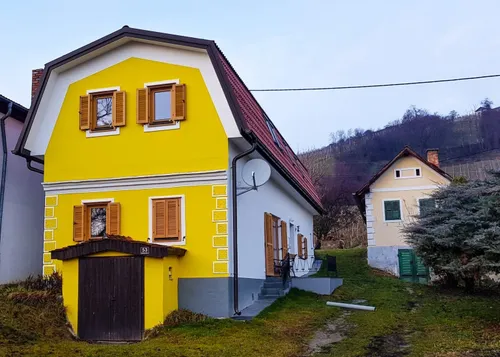 Ein gelbes Haus mit rotem Dach und braunen Fensterläden. Ein kleines Haus mit grünen Fensterläden steht in der Nähe.