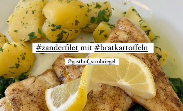 Ein Teller mit gegrilltem Zanderfilet, begleitet von Bratkartoffeln und einer Zitronenscheibe. Hashtags zeigen #zanderfilet mit #bratkartoffeln und @gasthof_strohriegl.