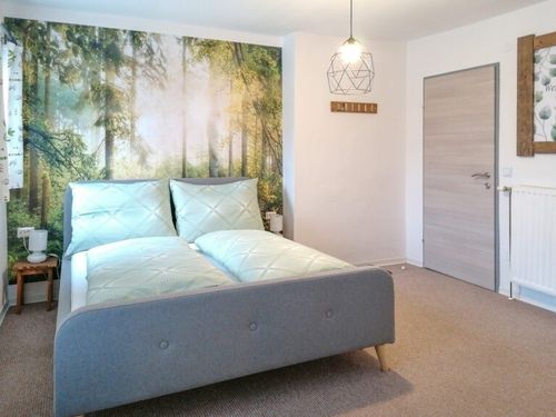 Ein Schlafzimmer mit einem Bett, Kissen und einer großen Wandmalerei eines Waldes. Ein Nachttisch mit einer Lampe steht neben dem Bett.
