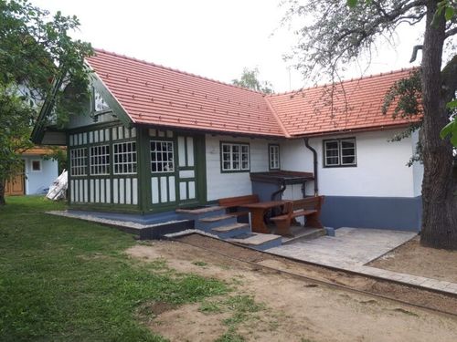 Ein weißes Haus mit rotem Dach und grünen Verkleidungen, eine Holzbank auf der Veranda und ein kleiner Garten mit Gras.
