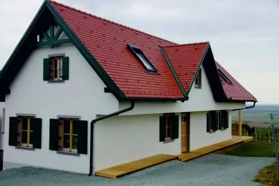 Ein weißes Haus mit rotem Dach und grüner Einfassung hat Holzläden und eine Holzveranda.