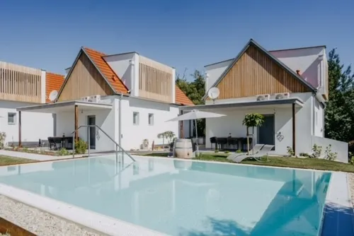 Ein modernes weißes Haus mit orangefarbenem Dach verfügt über einen großen Swimmingpool und einen Rasenbereich mit Liegestuhl und Sonnenschirm.