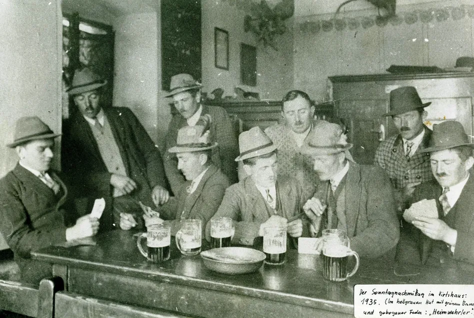 Schwarz-Weiß-Foto von Männern, die in einem Barraum an einer Bar sitzen, Bier trinken und rauchen.