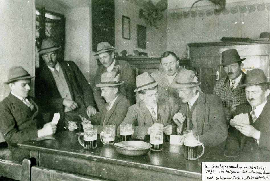 Schwarz-Weiß-Foto von Männern, die in einem Barraum an einer Bar sitzen, Bier trinken und rauchen.