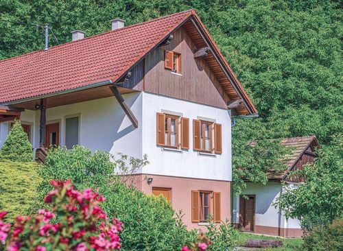 Ein gemütliches zweistöckiges Haus mit rotem Ziegeldach und Holzakzenten liegt eingebettet inmitten leuchtender Blumen und Grünpflanzen, mit einem kleineren Haus im Hintergrund sichtbar.