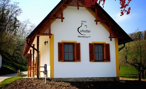 Ein kleines Haus mit gelb-weißer Außenfassade, mit schwarzem und weißem Logo über der Tür, zwei Fenstern mit braunen Fensterläden und einer Lampe über der Tür.