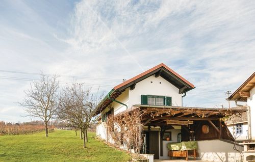 Ein weißes Haus mit rotem Dach steht auf einem grünen Feld. Das Haus hat eine Holzveranda, grüne Fensterläden und einen Holzfass an der Wand.
