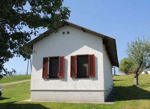 Ein kleines weißes Haus mit roten Fensterläden und einem grünen Rasen. Es hat zwei Fenster mit roten Fensterläden an der Vorderseite.