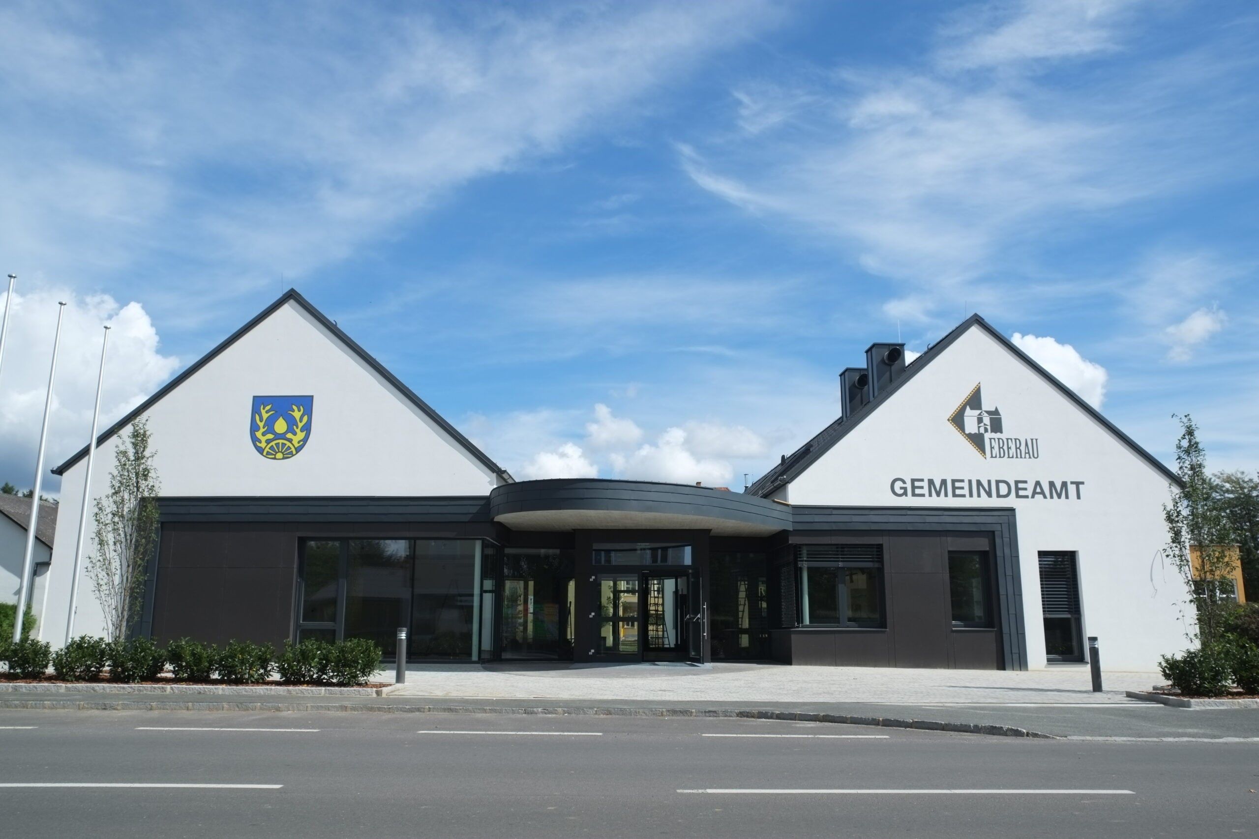 Die Vorderseite eines modernen Gebäudes mit einem blau-gelben Emblem und der Aufschrift Gemeindeau an der Fassade.
