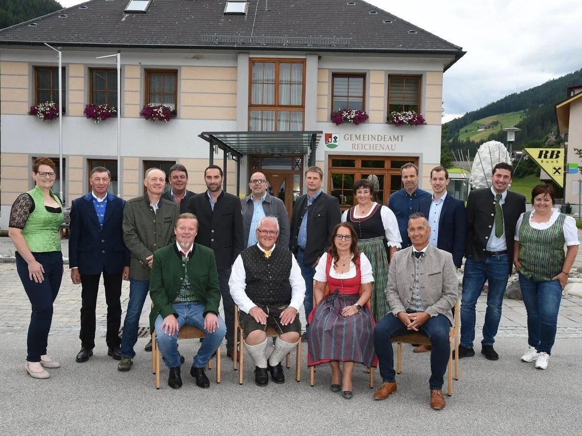 Eine Gruppe von Menschen in traditioneller Kleidung posiert für ein Foto vor einem Gebäude mit dem Schild Gemeindeamt Reichenau.