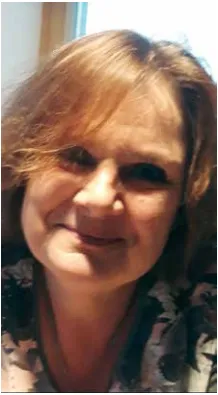 Eine lächelnde Frau mit kurzen, gewellten blonden Haaren, die ein Top mit Blumenmuster trägt, schaut direkt in die Kamera.