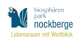 Das Logo des Biosphärenparks Nockberge. Es zeigt einen blauen Vogel mit ausgebreiteten Flügeln und einem Slogan 'Lebensraum mit Weitblick'. Der Text ist blau mit gelbem Umriss.