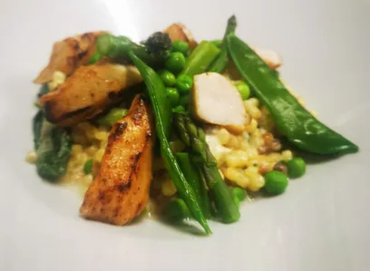 Ein Teller mit gegrilltem Hähnchen, Spargel, Erbsen und Reis mit einer Garnitur aus grünen Bohnen auf einer weißen Oberfläche.